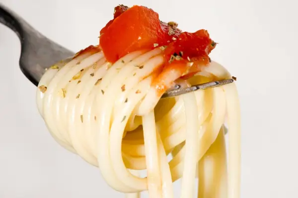 Eine Gabel mit Spaghetti, belegt mit Tomaten und Kräutern. Ein Vorgeschmack auf die besten italienischen Pasta Rezepte.