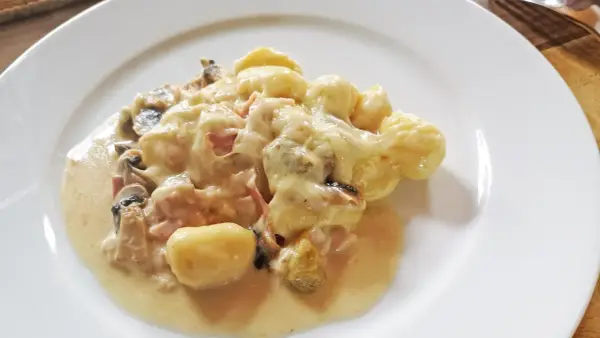 Gnocchi al forno mit cremiger Käsesauce, Pilzen und Schinken auf einem weißen Teller.