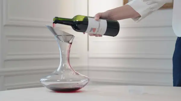 Roter Wein wird aus einer Flasche in einen Dekanter gegossen. Der Wein ist verkorkt und bereit zum Genießen.
