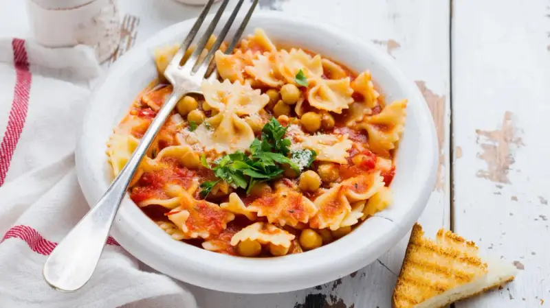 Farfalle-Pasta mit Kichererbsen in Tomatensauce, garniert mit Petersilie und Parmesan. Ein einfaches ceci rezept, perfekt für ein schnelles Mittagessen.