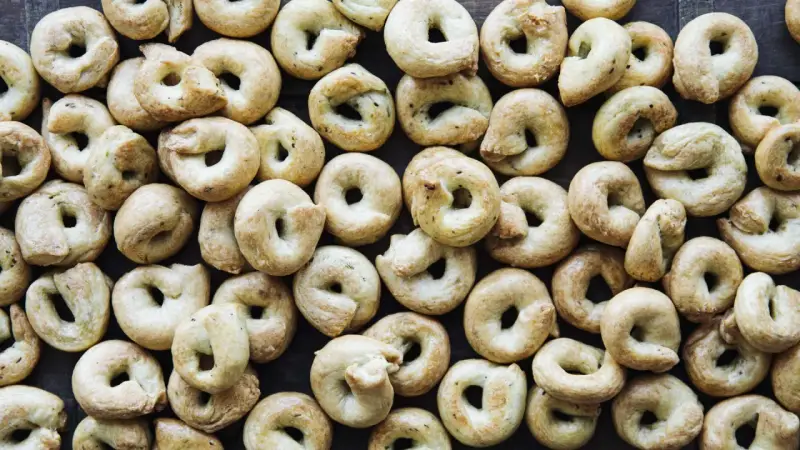 Viele goldbraune Taralli, die nach einem einfachen Taralli Rezept gebacken wurden, liegen dicht beieinander auf dunklem Holz.
