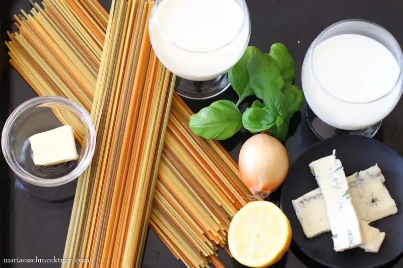 Zutaten für eine cremige Gorgonzola-Sauce: bunte Spaghetti, Butter, Zwiebel, Zitrone, Basilikum und Gorgonzola.