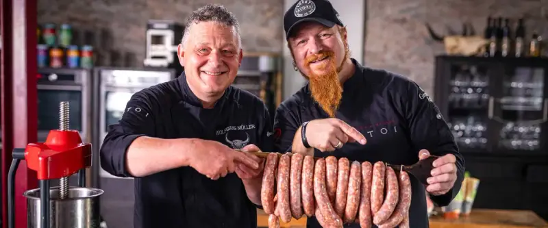 Zwei Metzger präsentieren stolz eine Reihe von frisch gefüllten Salsiccia mit Haut, bereit zum Braten.